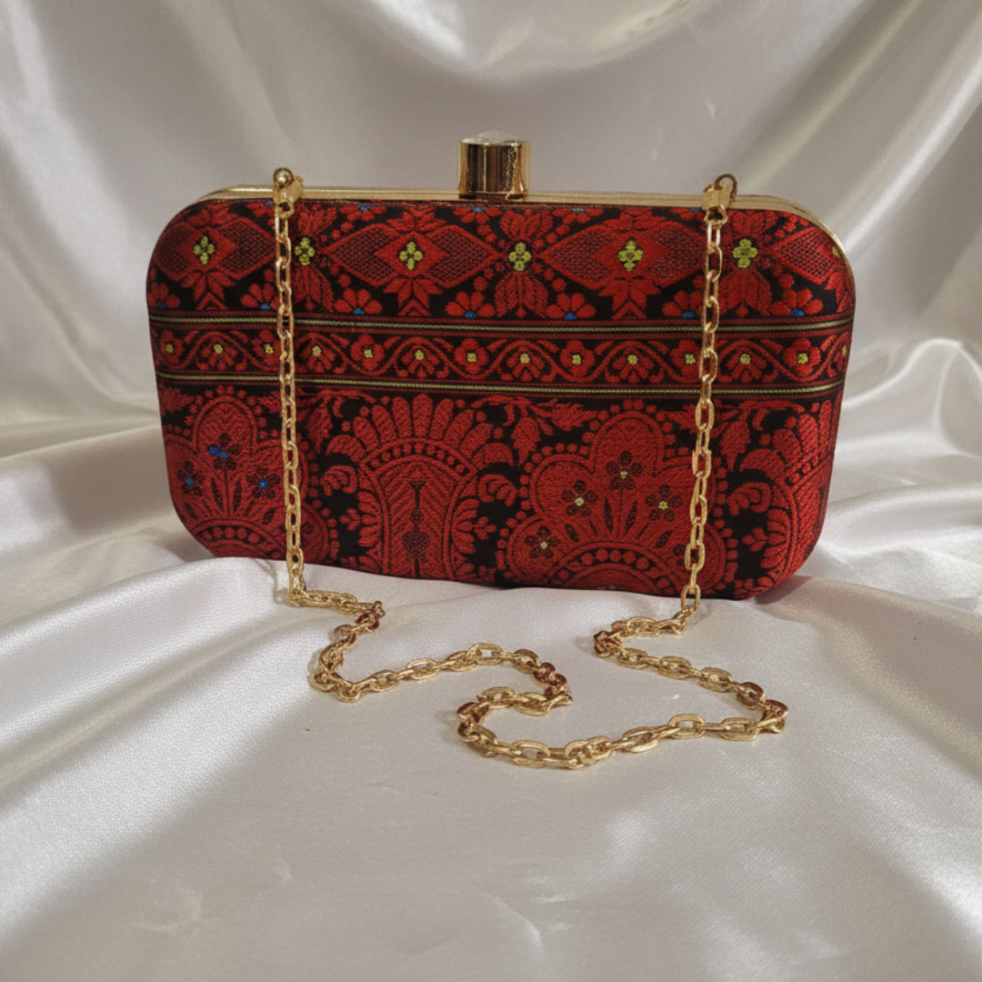 Red and black patterned handbag with gold chain on a white surface
