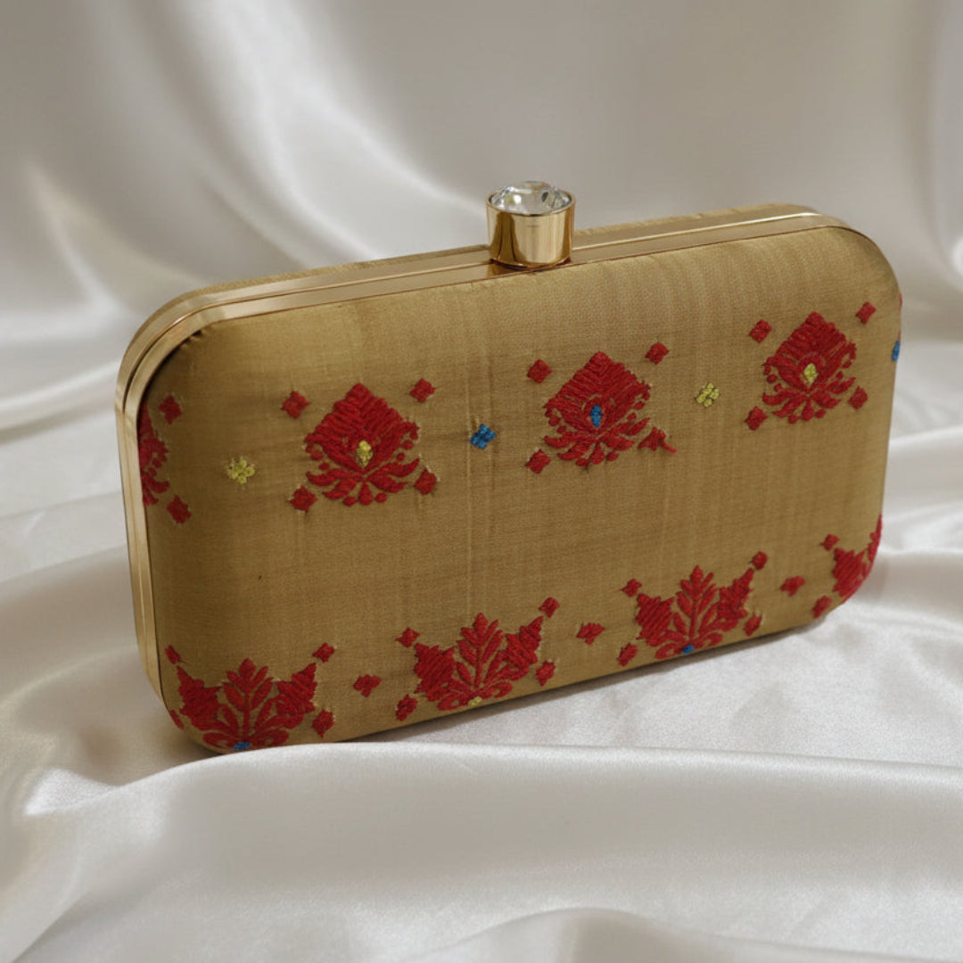Handwoven Assam silk clutch bag in antique gold colour with red traditional Assamese motifs and subtle multicolour detailing, featuring a metal clasp and structured frame